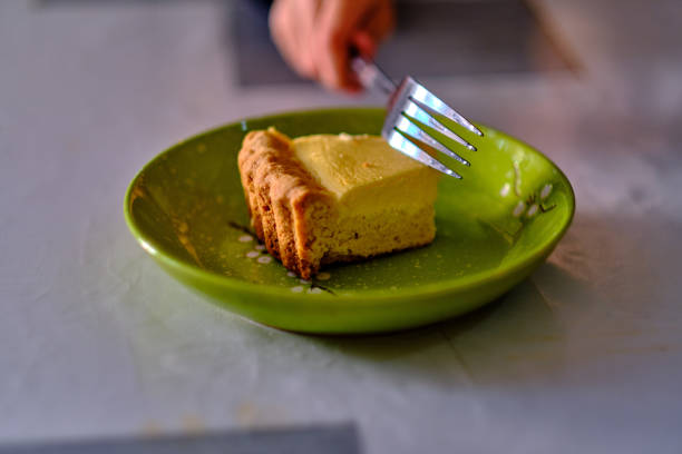 A piece of cheesecake on a green plate, from which a piece is being broken off with a fork.