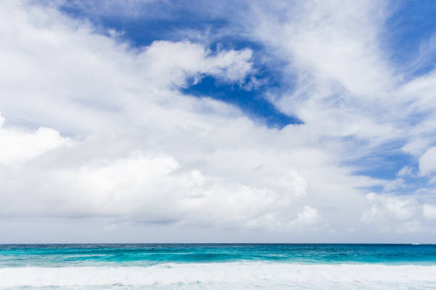 Peaceful ocean waters meet a vibrant blue sky adorned with beautiful white clouds, exuding calm and atmospheric beauty perfect for relaxation and inspiration