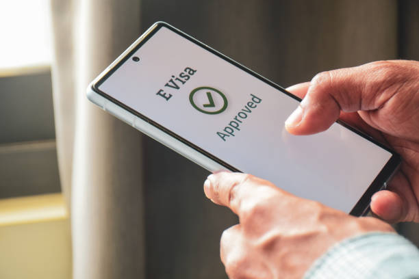 istock Man got notification about e-visa or electronic visa acceptance on his mobile phone. Office desk background, tourism, selective focus. 2202937801