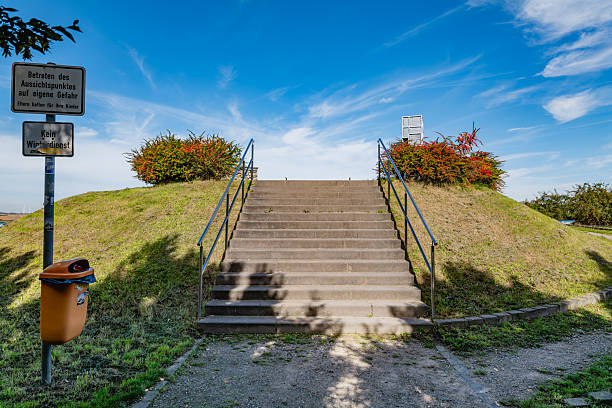 Staircase leading to a scenic observation point with warning signs, surrounded by lush greenery and a bright blue sky, inviting visitors to explore.