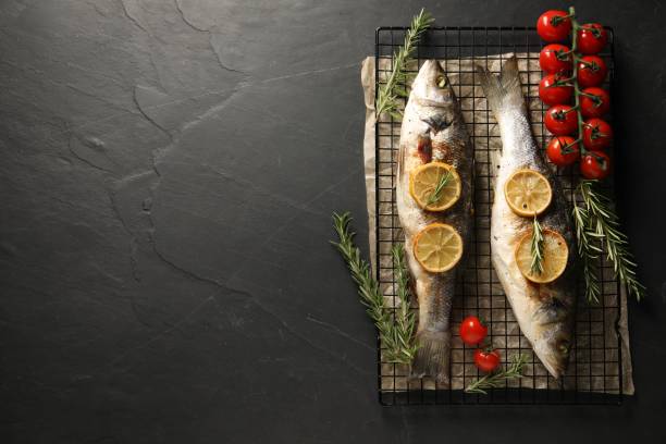 istock Baked fish with tomatoes, rosemary and lemon on black textured table, top view. Space for text 2202966548