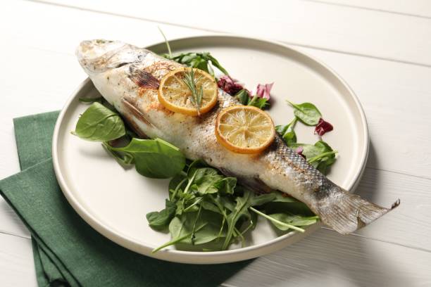 istock Baked fish with spinach and lemon on white wooden table, closeup 2202966552