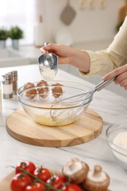 istock Woman whisking eggs while adding flour into bowl at light marble table indoors, closeup 2202966585