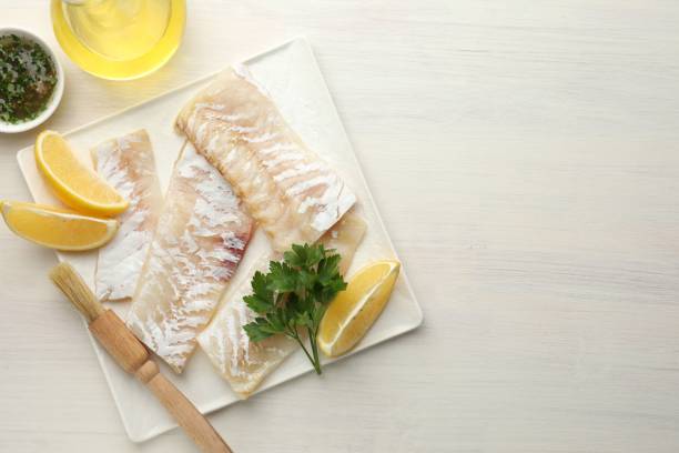istock Fresh raw cod fillets with spices and lemon on white wooden table, flat lay. Space for text 2202966598