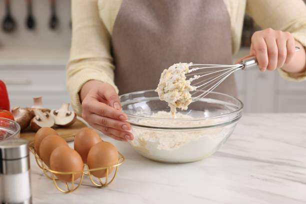 istock Woman making dough with whisk in bowl at light marble table, closeup 2202966620