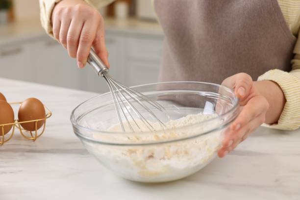 istock Woman making dough with whisk in bowl at light marble table, closeup 2202966685