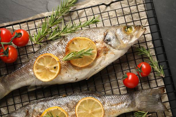 istock Baked fish with tomatoes, rosemary and lemon on black textured table, top view 2202966717