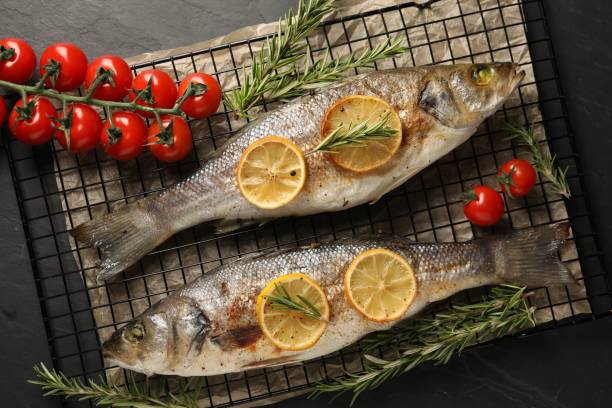 istock Baked fish with tomatoes, rosemary and lemon on black textured table, top view 2202966737