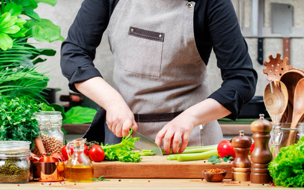 istock Private Chef cuts stalk green celery. Cozy kitchen with wooden table, kitchenware, vegetables, herbs and ingredients for cooking. Healthy vegan food, culinary, recipes, food blogging 2202967012