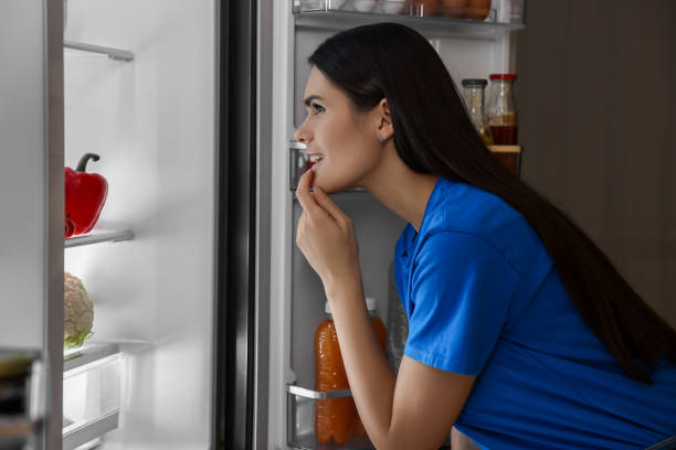 istock Thoughtful young woman looking into modern refrigerator at night 2202969593