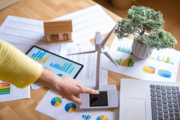 istock Businesswoman touching a small solar panel linked to a miniature wind turbine, surrounded by charts, graphs, and devices, representing investment in renewable energy 2202970383