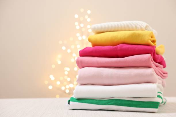 istock Stack of folded clothes on wooden table against beige background with blurred lights, space for text 2202972318