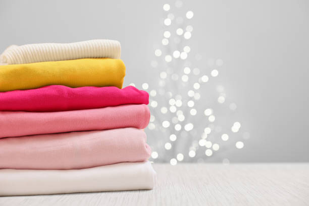 istock Stack of folded clothes on wooden table against beige background with blurred lights, space for text 2202972411