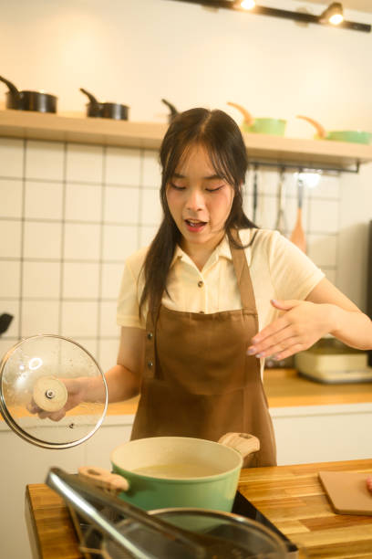 istock Young woman in brown apron lifting the lid off a pot while checking on boiling pasta 2202974929