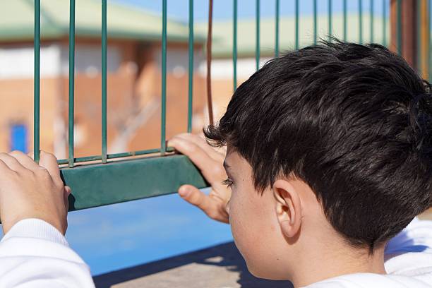 child leaning against a school gate, sad because of relationship or learning difficulties