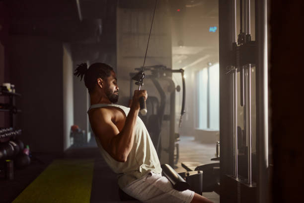 Black sportsman exercising on lat pull down machine in a gym.