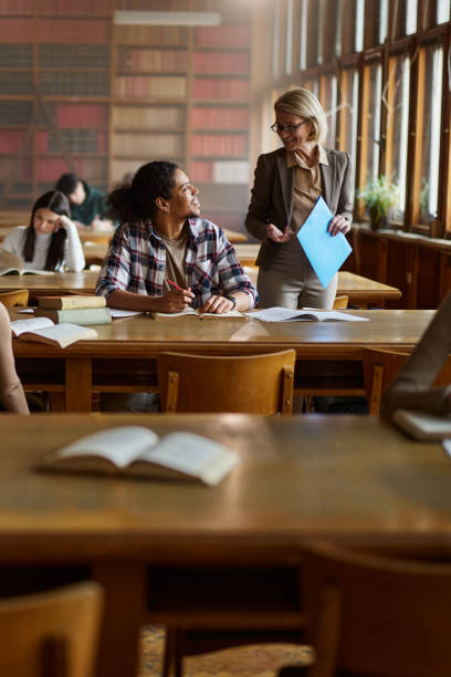 istock Happy senior professor talking to black student on a class in library. 2202978571