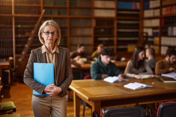 istock Serious mature professor with her students in library. 2202979045