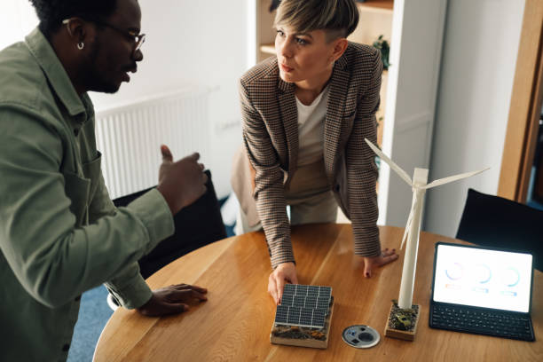 istock Engineers discussing green energy solutions with solar panel and wind turbine models 2202982620
