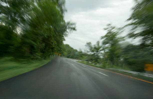 Blurred image of a road with green trees on both sides, suggesting motion.
