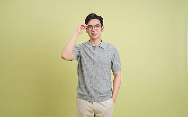 istock Young man adjusting glasses while standing against a soft green backdrop in an indoor setting 2202984213