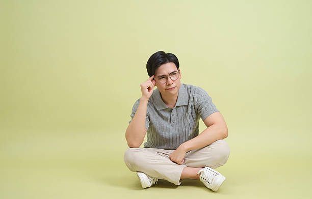 Thoughtful young man sitting cross-legged in a relaxed pose against a soft green background