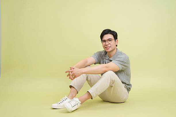 istock Young man sits casually against a light green background, showcasing a relaxed demeanor and stylish outfit during a photoshoot 2202984294