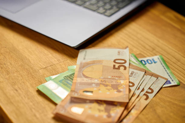 Euro banknotes and laptop on wooden table. Concept of cash payments, savings and personal finance