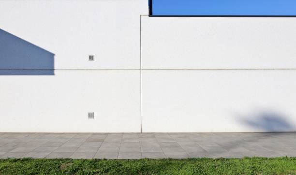 istock White concrete prefab wall with  stone tiled pavement and a strip of grass in front. 2202987995