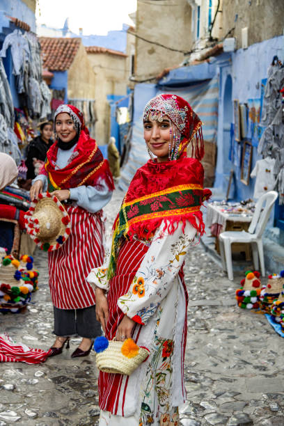 A festive scene in Chefchaouen showcasing women in traditional Moroccan clothing, surrounded by local crafts and the city's iconic blue walls.