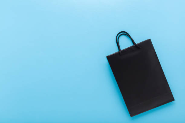 Dark black shopping paper bag on light blue table background. Pastel color. Closeup. Empty place for text. Top down view.
