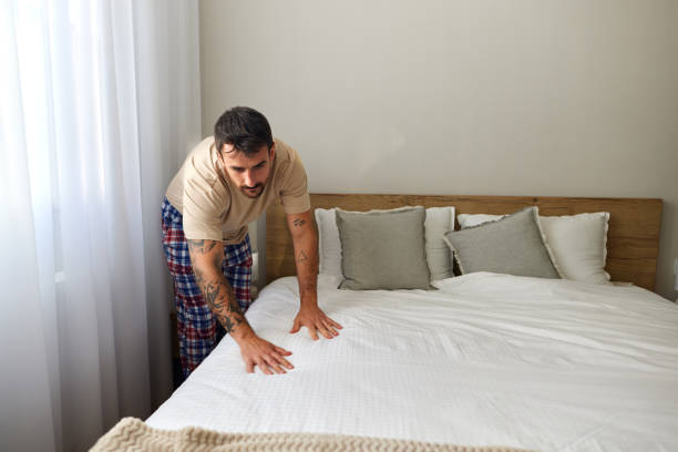 istock Young man making his bed in the morning. 2202989710