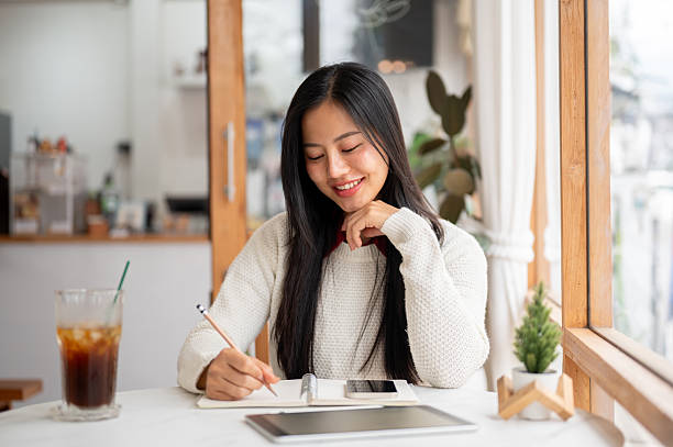 istock An asian woman is smiling while writing with a pencil on notebook with phone and tablet on the table 2202991684