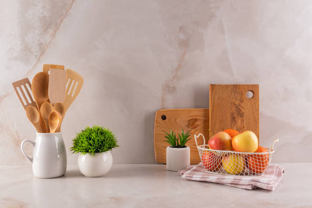 istock Beautiful kitchen backdrop with a set of wooden kitchen tools and cutting boards on a marble beige countertop with potted plants. A bowl of fruit. 2202994692