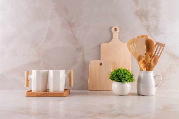 istock Two stylish white ceramic mugs, a cutting board set, a pitcher with wooden tools, and a potted flower on a marble countertop. kitchen background. 2202994694