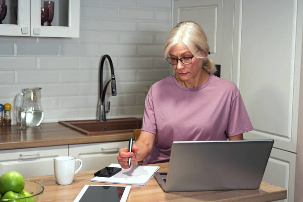 istock Elderly woman studying online while writing down important information 2203000118