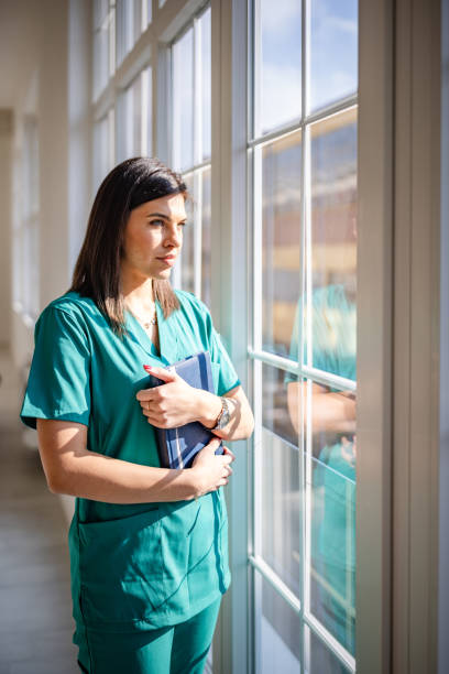 istock Young female nurse reflecting while standing by a window in a healthcare setting 2203000873