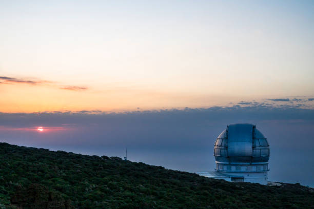 A large telescope is on a hillside, with the sun setting in the background