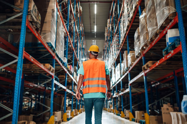 istock Warehouse worker walking through large warehouse with high shelves full of goods 2203001504
