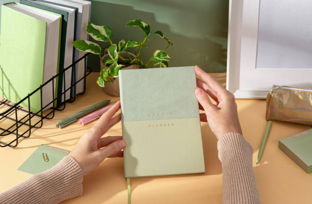 istock Women's hands show elegant lightgreen weekly planner with stationery, sticky notes, perfect for notes, sketches, and organizing thoughts.  Organized workspace, productive study setup. 2203002407