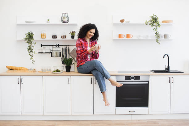 istock Smiling woman sitting on kitchen counter with modern decor 2203006509
