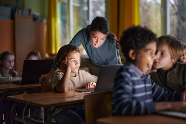 istock Female teacher assisting schoolboy with using laptop on a class. 2203007027