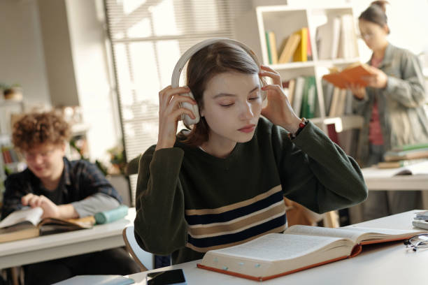 Woman Putting on Headphones Studying in School Library
