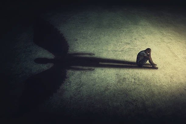 istock Depressed young man sitting alone isolated in a dark room, casting a shadow of a powerful guardian angel. Inner strength conceptual background. Stressed person introvert with an imaginary friend 2203018429