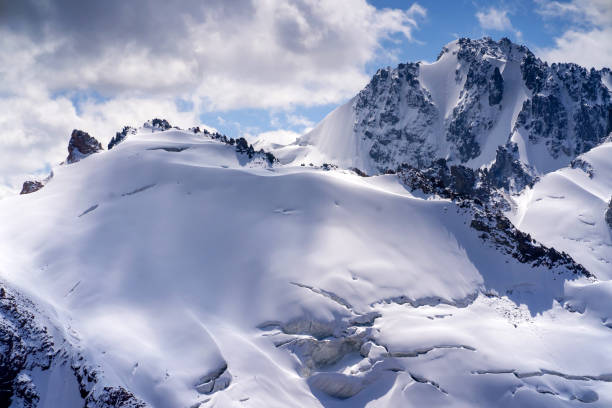 Harsh majestic landscape with snow-capped mountains, glacier and ice cracks covered with snow on a sunny day.
