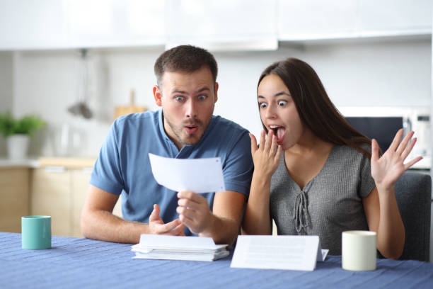 istock Amazed couple checking bank statement in the kitchen 2203018715