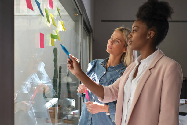 istock Multiracial female colleagues discussing project near wall with sticky notes 2203020150