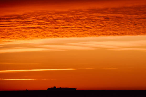 Winter dawn and colorful clouds, carrier ship silhouetted on horizon, Chesapeake Bay