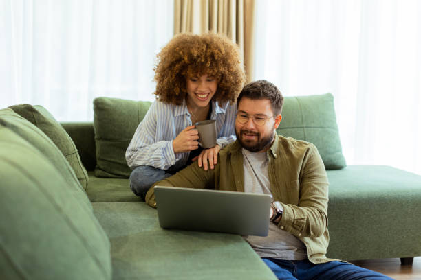 istock Couple sharing a joyful moment while exploring ideas on a cozy green couch in a sunlit living room 2203030863