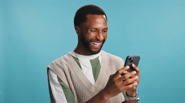 istock Online, black man and laughing with phone in studio for comic text message, social media meme or funny joke. Mockup space, person or happy with smartphone for communication or chat on blue background 2203034182